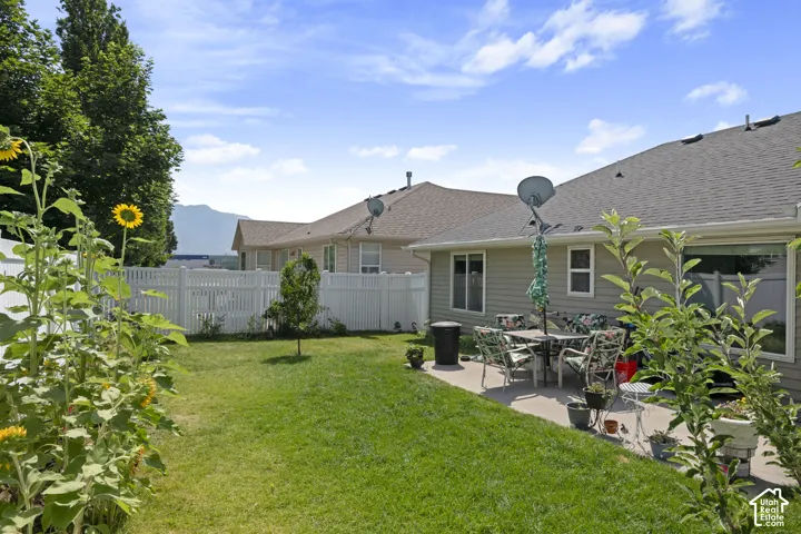 Manicured lawn with a white vinyl fence, mature trees, and a concrete patio