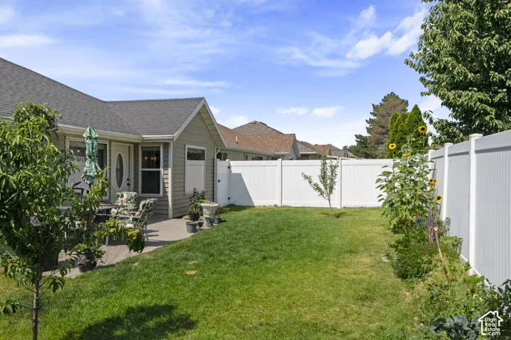 Expansive backyard featuring a manicured lawn, a concrete patio, and a white privacy fence