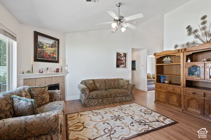 Vaulted ceilings, wood-finish flooring, ceiling fan, and a tiled fireplace with mantel