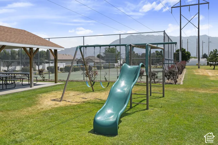 Playground with slide and swings, featuring a nearby covered picnic area, green lawn, and distant mountains