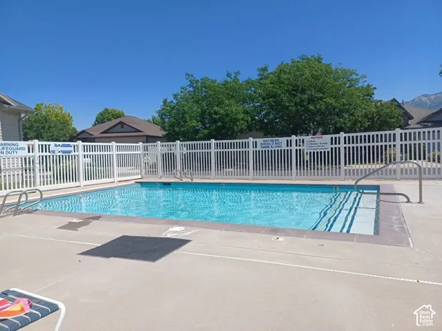 Outdoor swimming pool with concrete decking, white picket fencing, and surrounding green trees