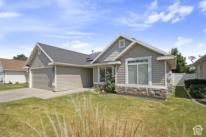 Exterior featuring horizontal siding, stone veneer accents, an attached garage, a paved driveway, and a fenced side yard