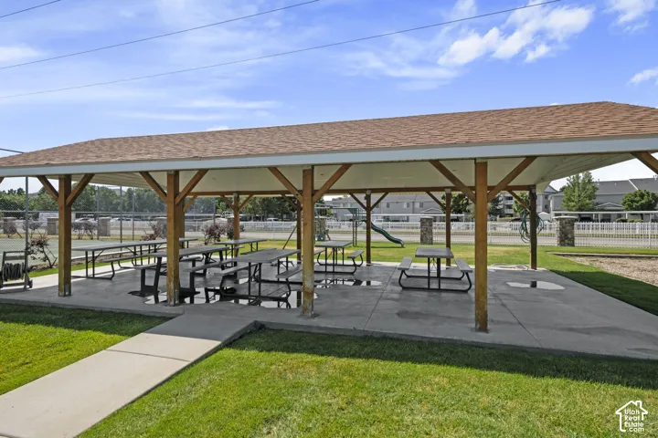 Covered picnic area with multiple tables, concrete slab, wood support beams, and asphalt shingle roof