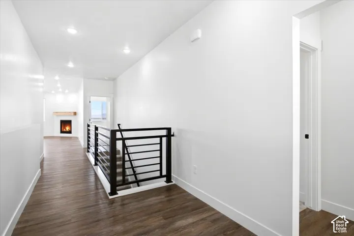 Wood-finish flooring throughout, recessed ceiling lighting, contemporary black metal stair railing, and a fireplace with a light wood mantel