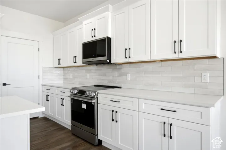 White shaker-style cabinetry with matte black hardware, stainless steel range, built-in microwave, light-toned countertops, and subway tile backsplash