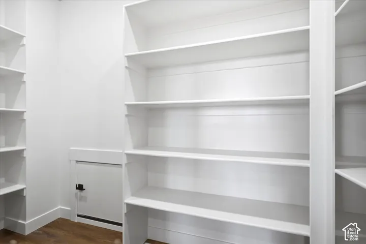 Built-in white shelving, wood-finish flooring, white walls, and a white access panel