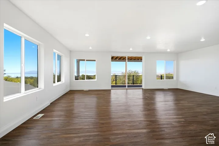 Spacious room featuring wood-finish flooring, multiple large windows, recessed lighting, and a glass sliding door opening to an exterior balcony with a railing