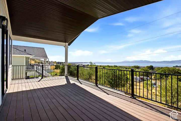 Expansive covered deck with wood-finish flooring, black metal railings, and a distant body of water