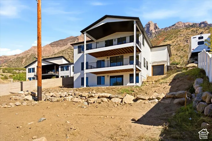 Multi-level home featuring white horizontal siding, black-framed windows, and three separate balconies with black railings