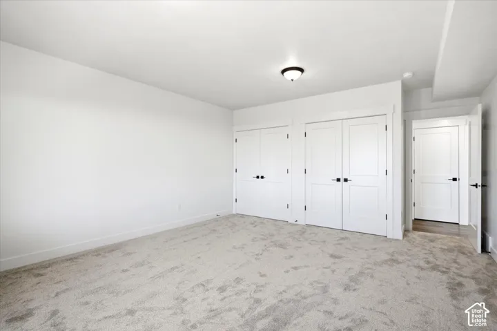 Light-toned wall-to-wall carpeting, white walls, multiple panel doors with black hardware, and a semi-flush mount ceiling light fixture