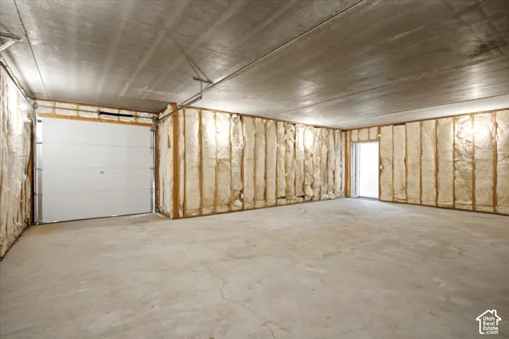 Concrete flooring, exposed ceiling, insulated wall framing, white overhead garage door, and an interior door