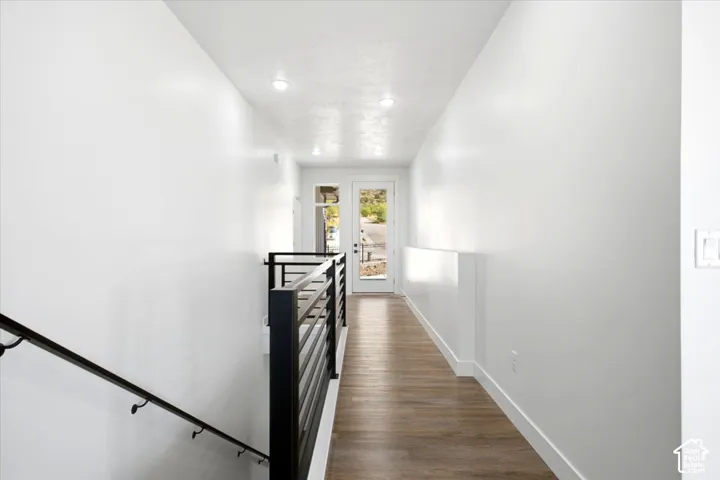 White walls, recessed lighting, wood-finish flooring, and black metal stair railing