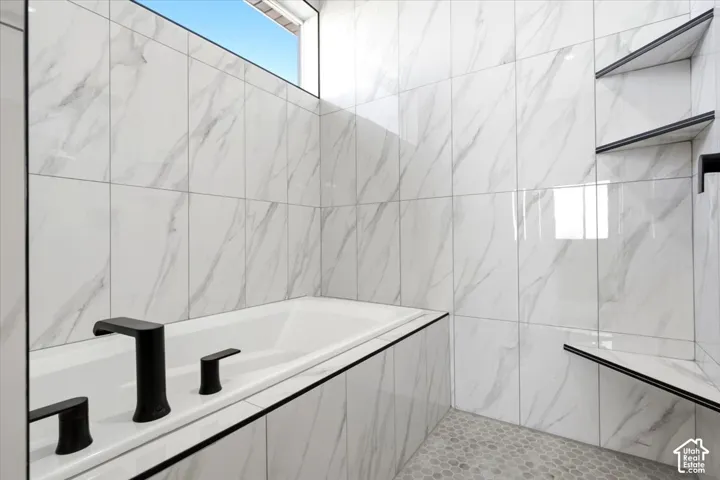 Integrated bathtub featuring matte black fixtures, full-height wall tiling, a high transom window, and built-in shelving