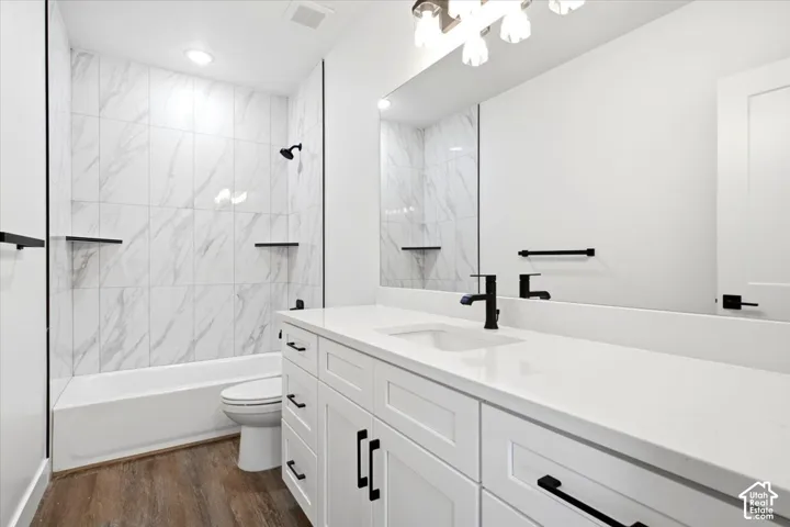 Modern bathroom featuring a white tub with marble-look tile surround, white vanity with integrated sink, black hardware, and wood-finish flooring
