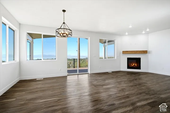 Expansive wood-finish flooring, contemporary fireplace with a wood-beam mantel, recessed lighting, and a modern chandelier