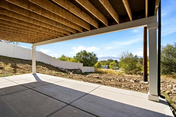 Covered patio with a concrete slab, supported by white columns, and framed by a white privacy fence