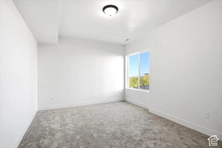 Bright room with neutral wall paint, gray patterned carpeting, a large window, and a flush mount ceiling light