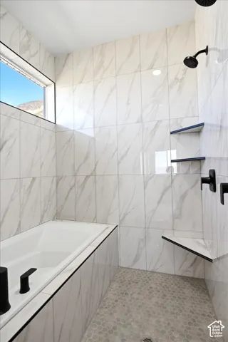 Built-in bathtub and shower area featuring large format wall tiles, pebble tile flooring, matte black fixtures, and a high horizontal window