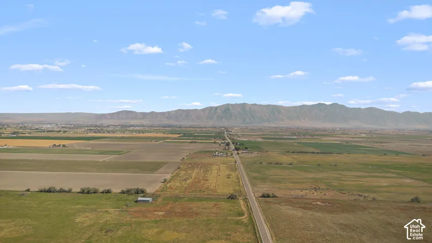 Expansive rural landscape featuring a paved road, agricultural fields, and distant mountain ranges