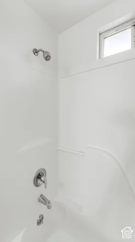 White tub and shower combination with chrome fixtures and an overhead window