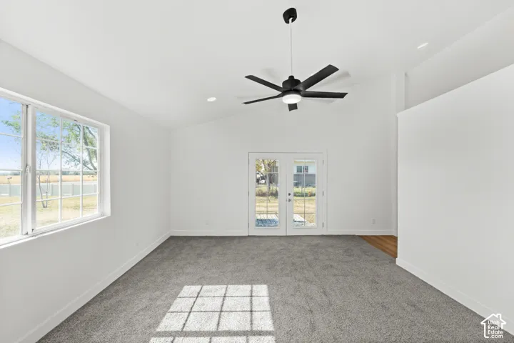 Vaulted ceiling with a contemporary ceiling fan, dual French doors with integrated blinds, and light gray carpeting