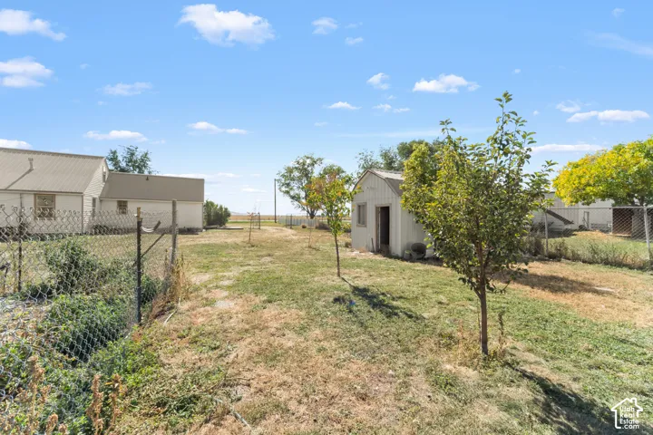 Expansive exterior space featuring a chain-link fence, mature trees, and a detached outbuilding