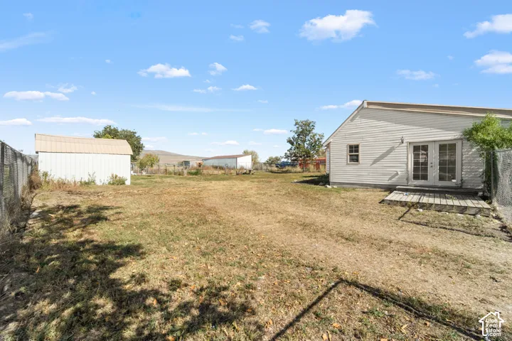 Expansive outdoor space featuring a detached storage shed, chain-link fencing, and a private rear entrance with French doors