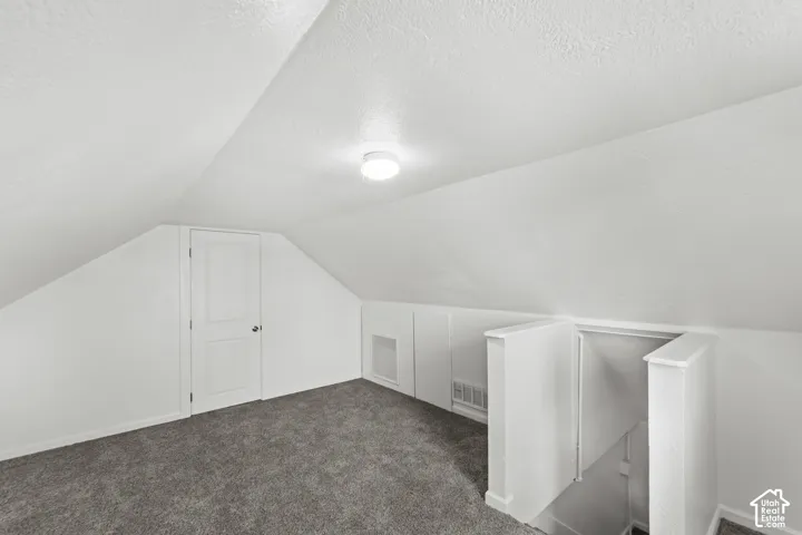 Carpeted attic space with sloped ceilings and a flush-mount light fixture