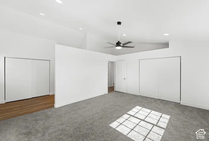 Vaulted ceiling with recessed lighting, ceiling fan, plush carpet, wood-finish flooring, and two sliding door closets