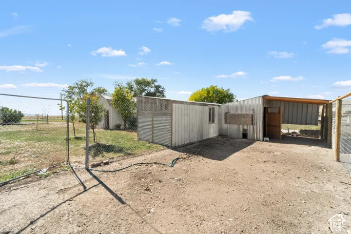 Chain link fencing enclosing a dirt and grass area, featuring a metal-sided outbuilding with a partially covered outdoor structure