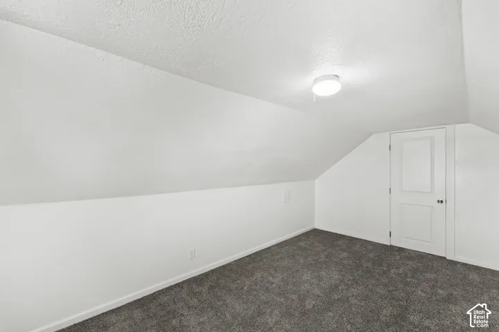 Sloped ceiling with recessed lighting, plush grey carpeting, white paneled door, and neutral wall tones