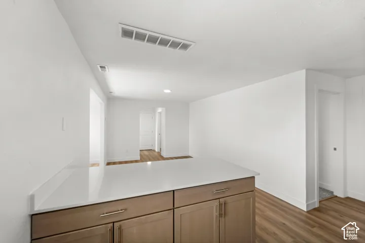 Wood-finish flooring throughout, white walls, recessed ceiling lighting, light wood-tone cabinetry, and a light-toned countertop