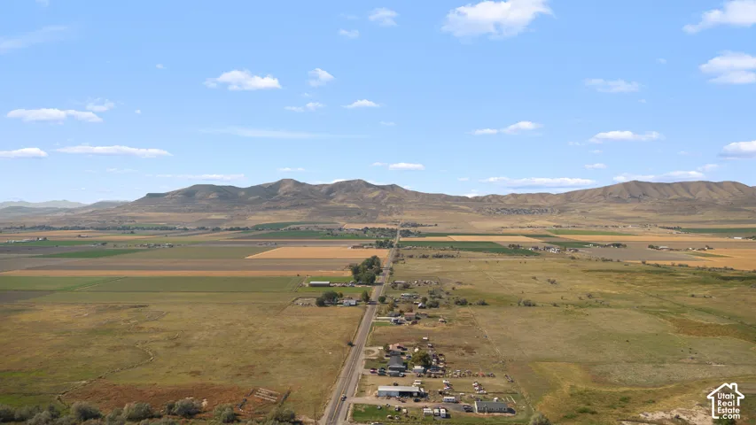 Expansive agricultural land featuring a paved road, scattered structures, and distant mountains