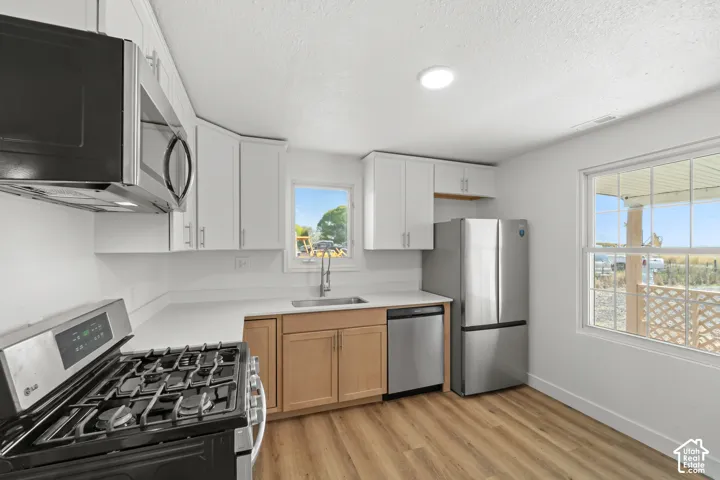 Kitchen featuring white cabinetry, stainless steel appliances, wood-finish flooring, light countertops, and a window with natural light
