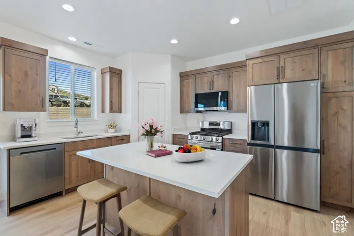 Kitchen featuring wood-finish cabinetry, stainless steel appliances, a center island with a light-toned countertop, and recessed lighting
