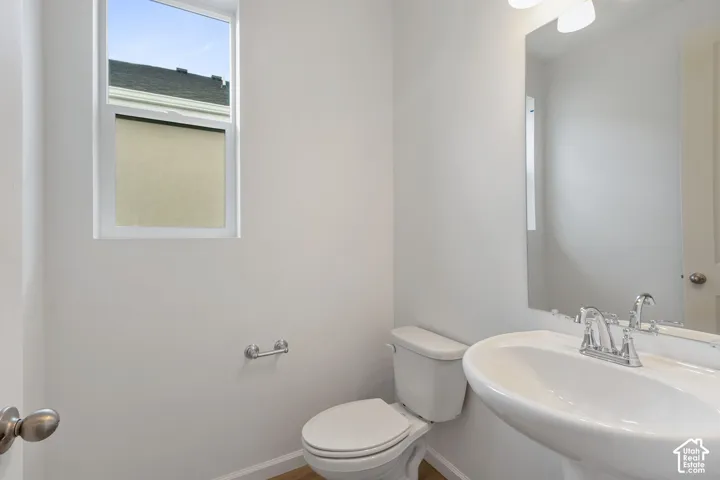 Pedestal sink with chrome fixtures, an overhead vanity light, an elongated toilet, and a window with privacy film