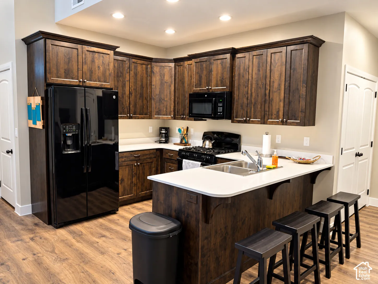 Kitchen featuring stained wood cabinetry, solid-surface countertops, integrated breakfast bar, wood-finish flooring, and recessed lighting