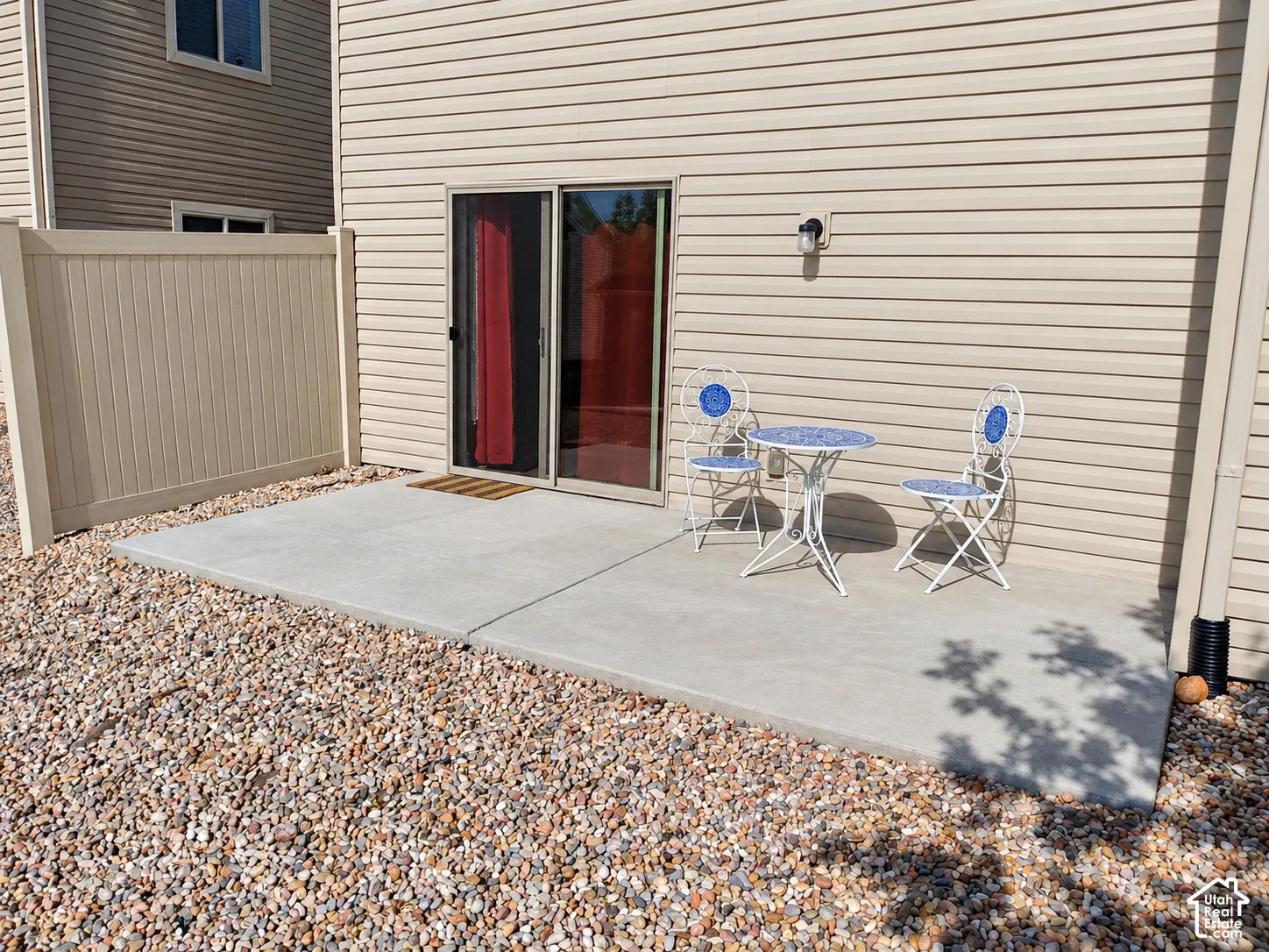 Concrete patio featuring tan vinyl siding, a sliding glass door, and a solid-panel privacy fence