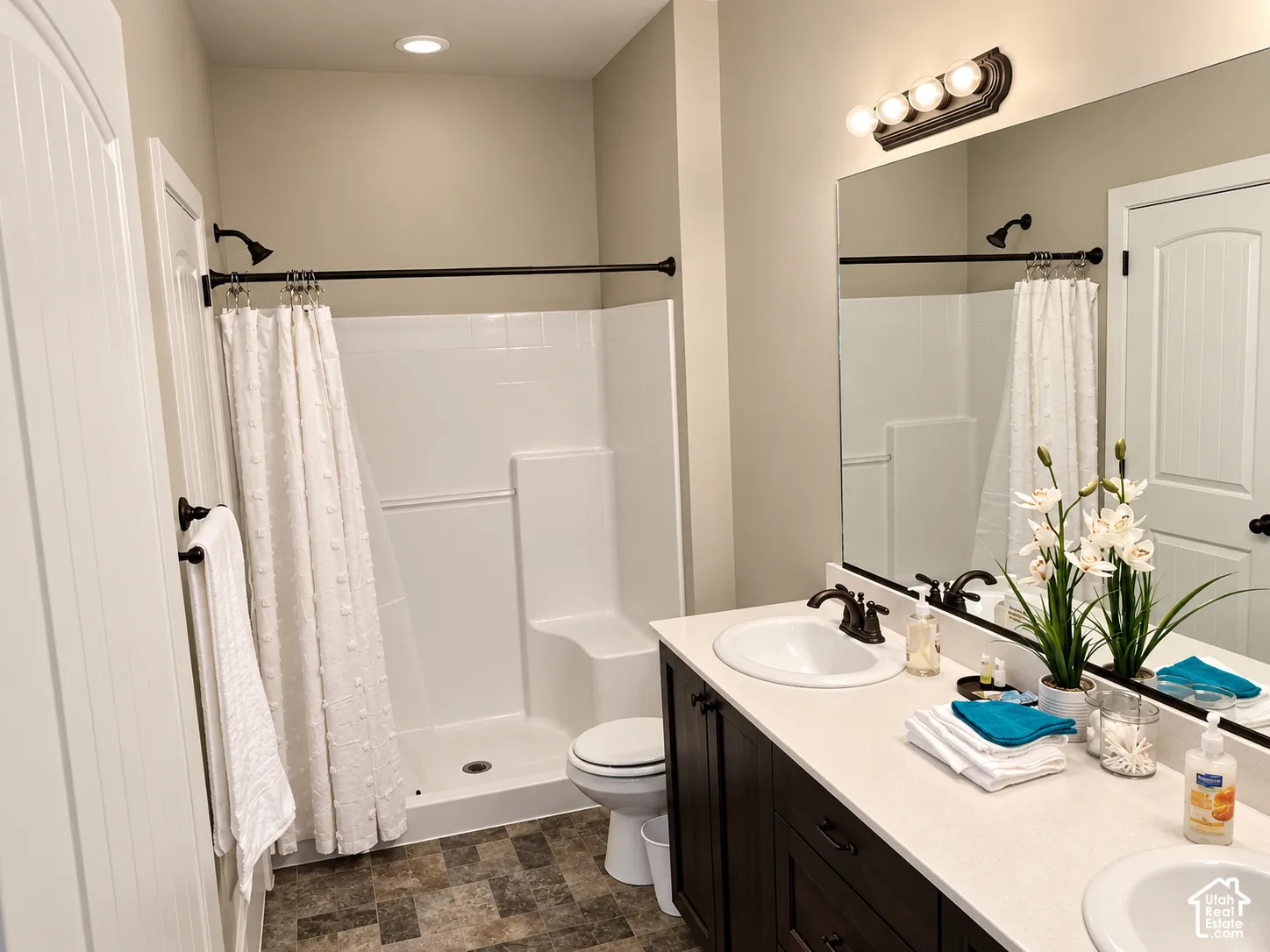 Bathroom featuring a dual-sink vanity with dark cabinetry, light-toned solid surface countertop, inset mirrors, and a separate stall shower with built-in bench seating