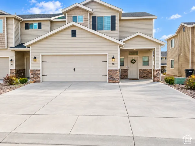 Multi-level exterior featuring light-toned horizontal siding, stone veneer accents, an attached two-car garage, and a covered entryway
