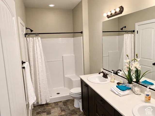 Bathroom featuring a dual-sink vanity with dark cabinetry, light-toned solid surface countertop, inset mirrors, and a separate stall shower with built-in bench seating