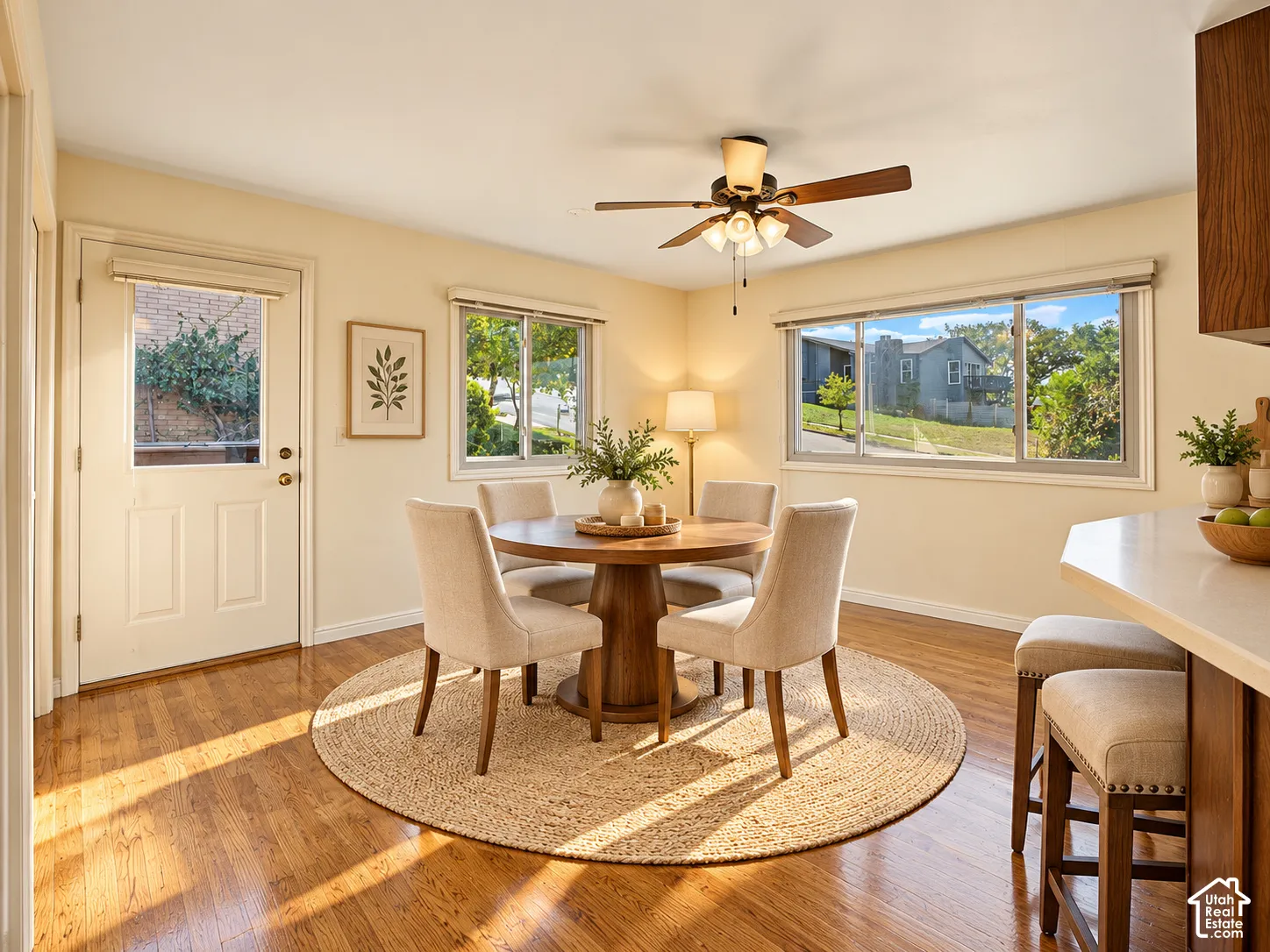 Wood-finish flooring, ceiling fan with integrated lighting, multiple windows, and a built-in breakfast bar with stools