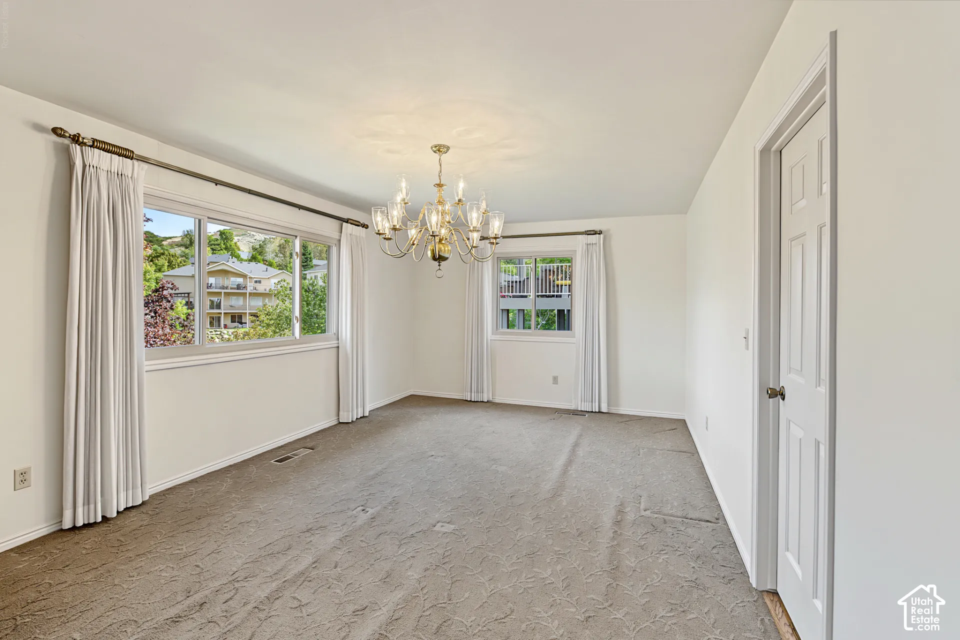 Recessed lighting, ornate brass chandelier, multiple windows, white painted walls, and a white interior door