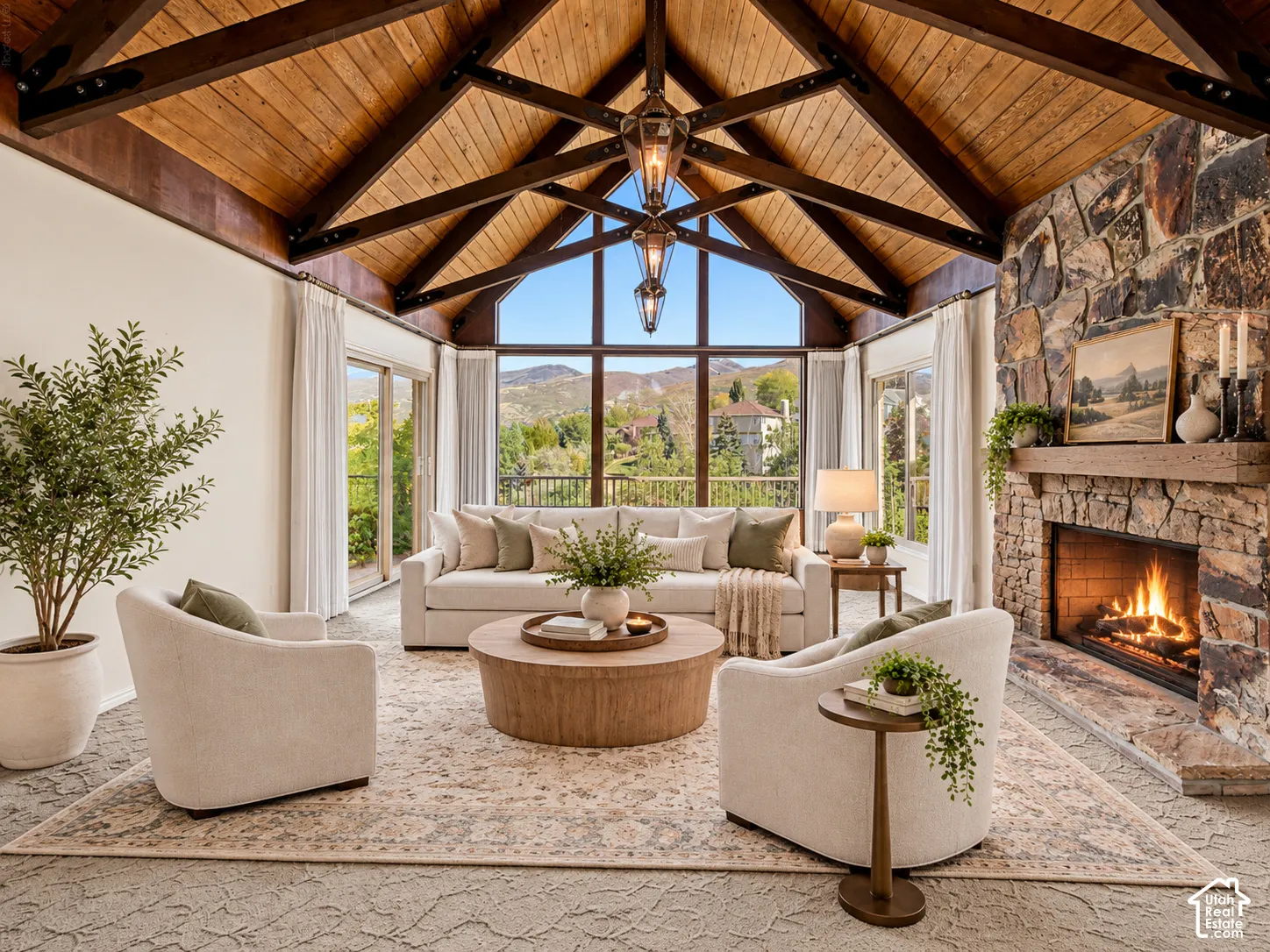 Vaulted wood-paneled ceiling with exposed beams, full-height stone fireplace, large picture windows, and sliding glass doors