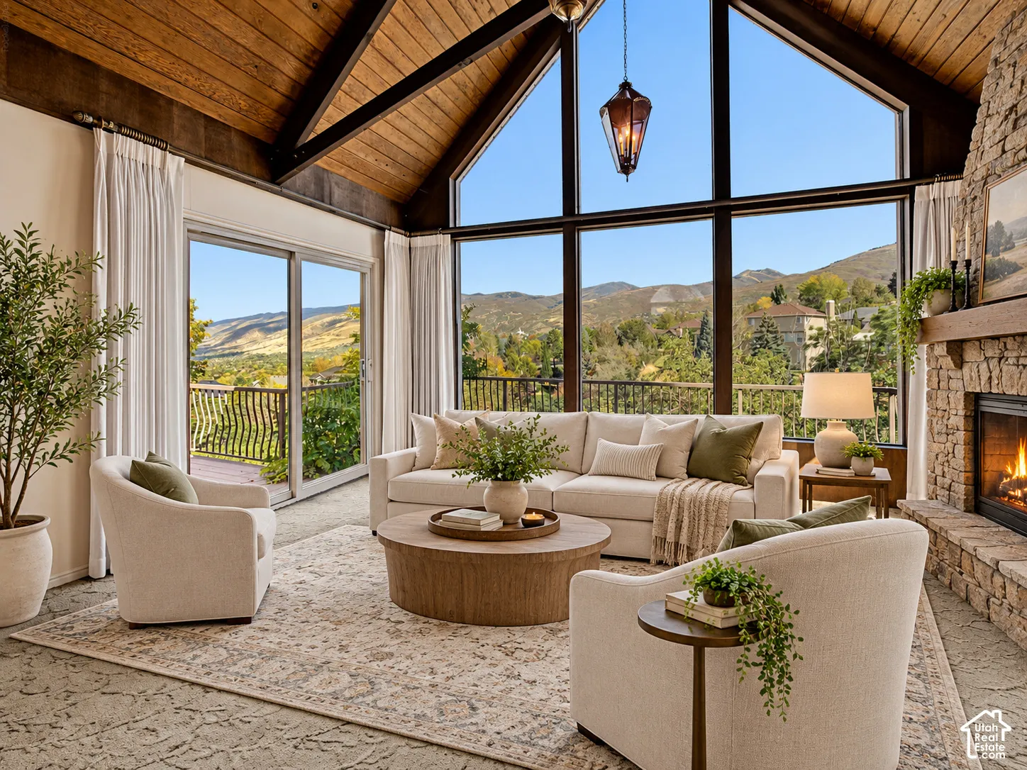 Vaulted wood-paneled ceiling, floor-to-ceiling windows, stone-clad fireplace with wood mantel, sliding glass door to exterior, and exterior balcony with metal railing