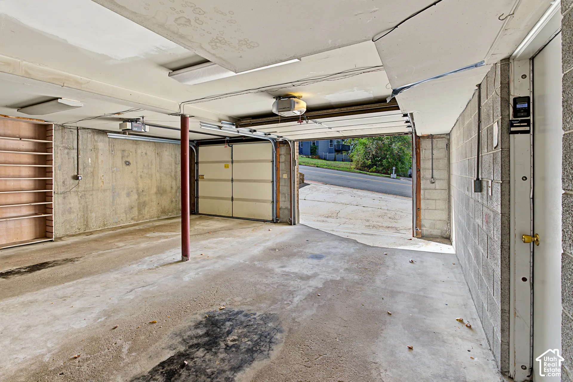 Concrete block walls, concrete flooring, overhead lighting, built-in shelving, and an automatic garage door opener