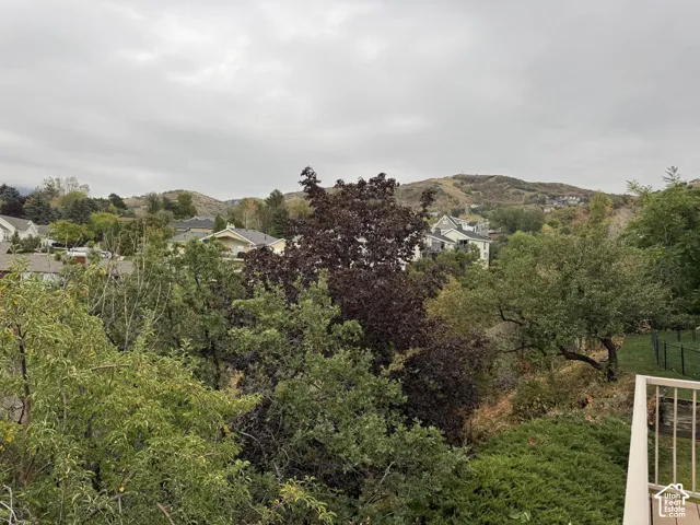 Elevated balcony with a beige metal railing overlooking mature trees, dense vegetation, and a mountain backdrop