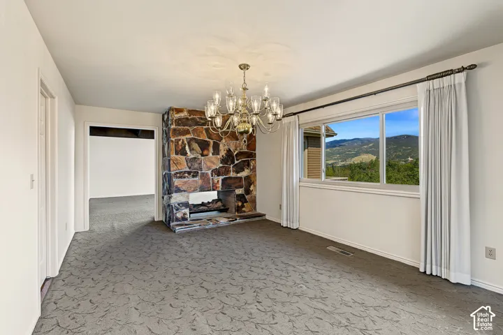 Stone-clad fireplace with built-in hearth, chandelier lighting fixture, picture window with outdoor scenery, and patterned carpeting