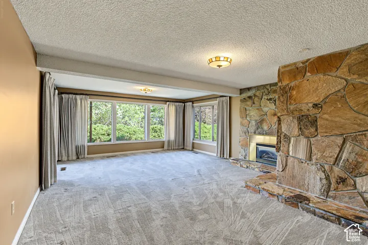 Spacious living area featuring a prominent stone fireplace, large windows, and neutral carpeting