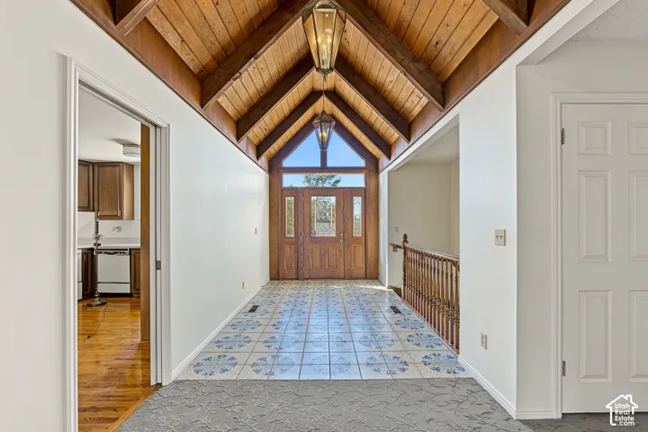 Vaulted wood-paneled ceiling with exposed beams, decorative tile flooring, wooden entry door with sidelights, and an upper transom window
